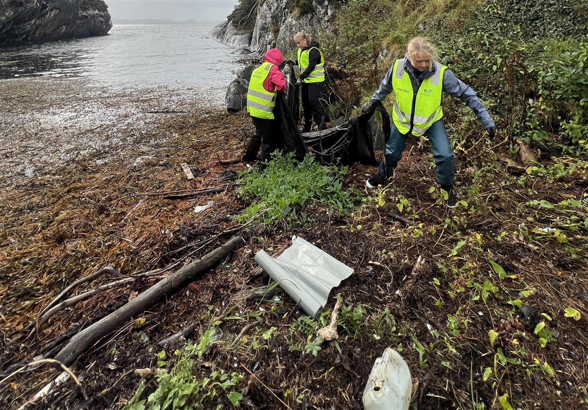 Tre damer med refleksvest plukker plastsøppel i sjøkanten - Klikk for stort bilde