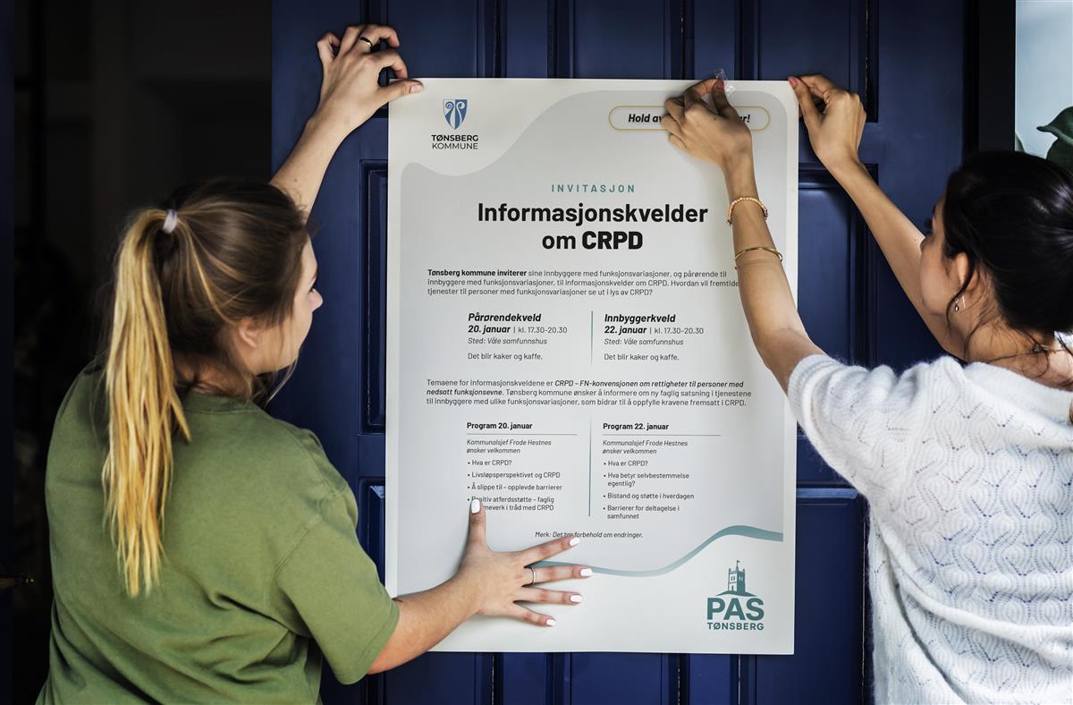 To personer henger opp informasjonsplakat - Klikk for stort bilde